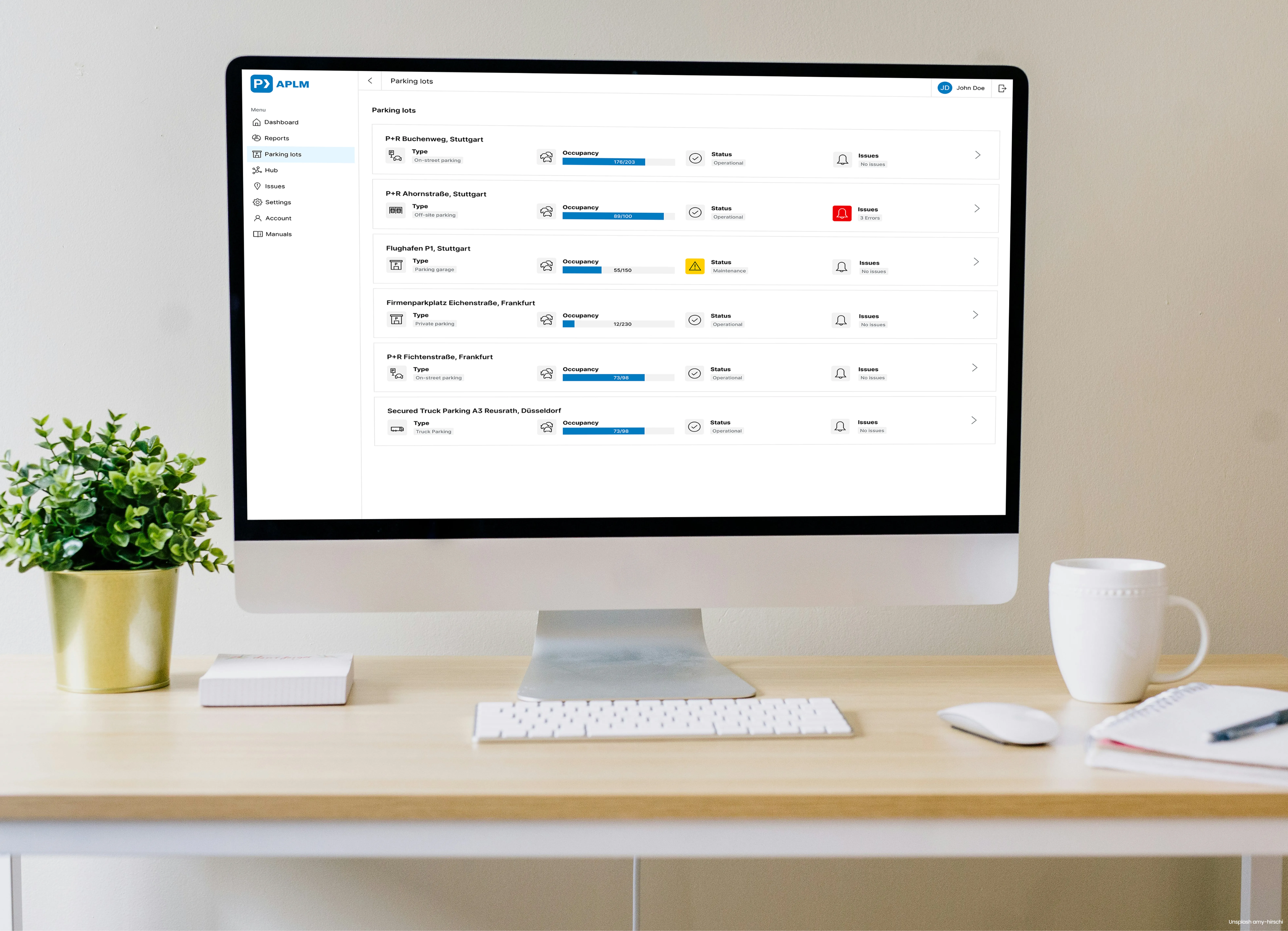 Desktop computer showing APLM web application user interface. On the monitor there is a list of parking lots with occupancy status displayed.